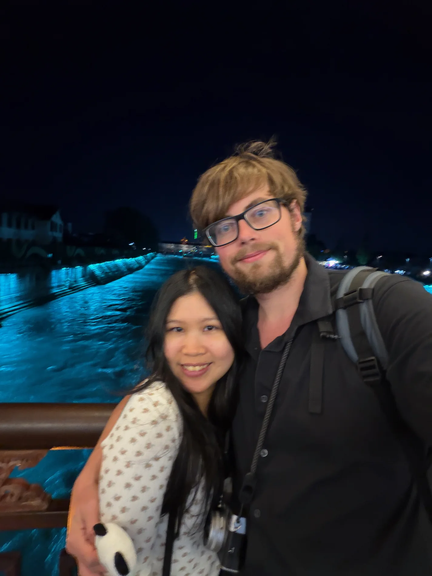 Lewis and Gail taking a happy selfie by blue-lit water at night.