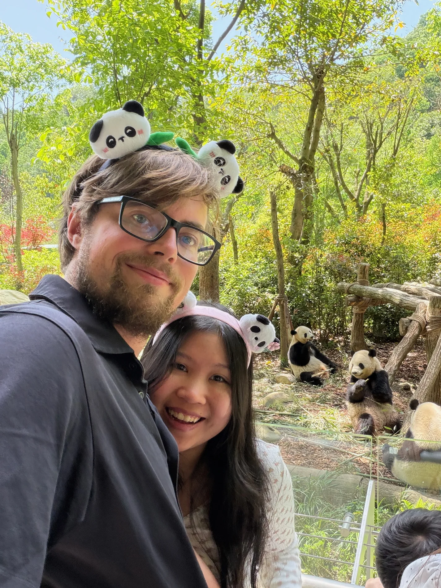 Lewis and Gail wearing panda headbands beside a group of pandas.