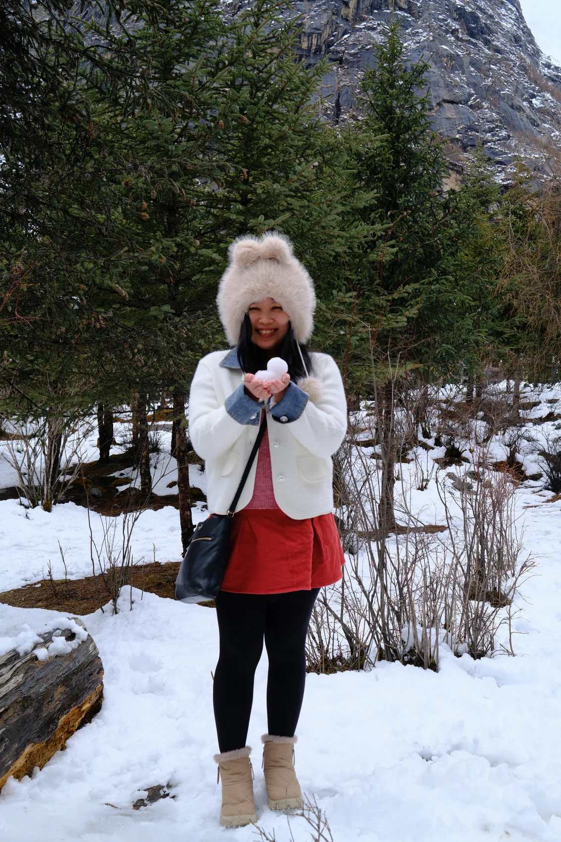 Gail holding a snowball beside a snowy forest.