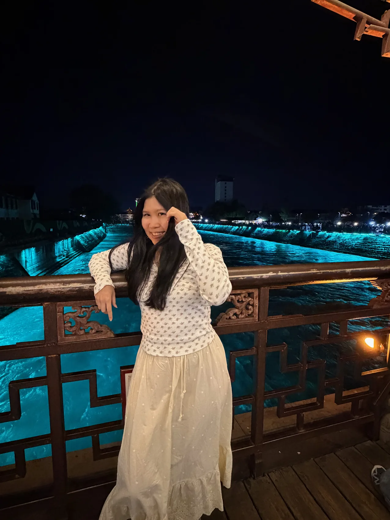 Gail standing on a bridge beside blue-lit water at night.