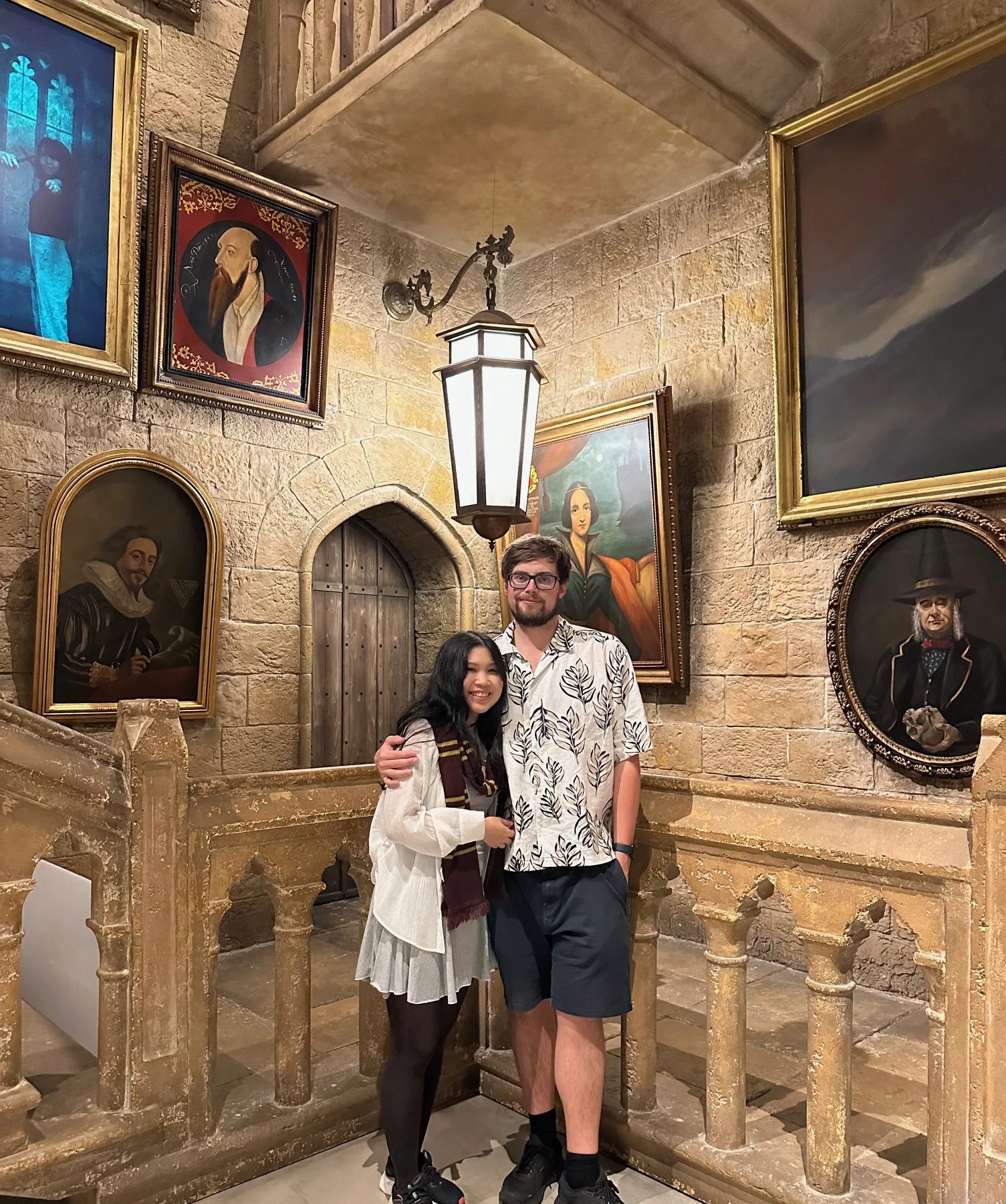 Lewis and Gail standing on a stone staircase lined with portraits.