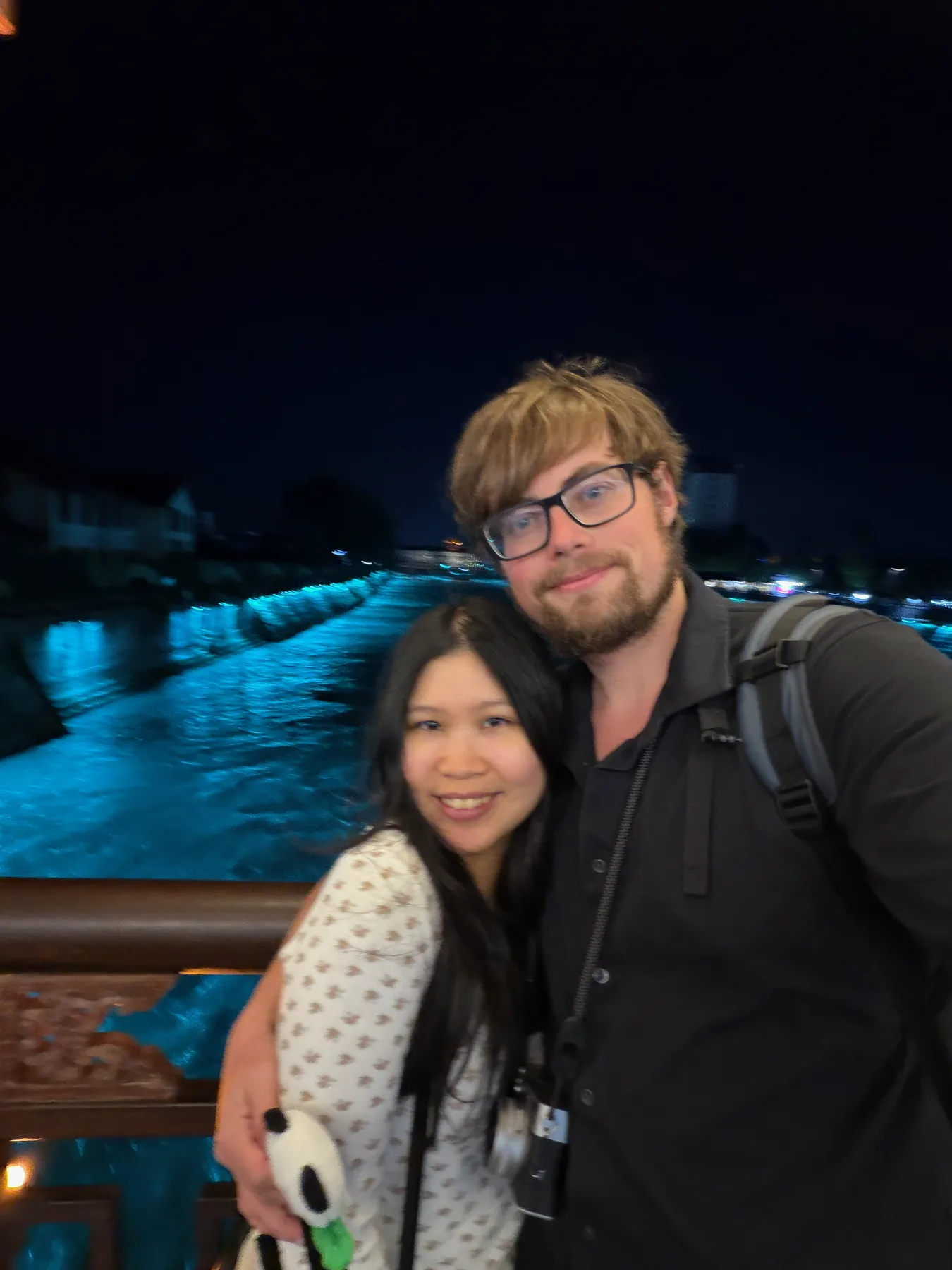 Lewis and Gail smiling together beside glowing blue water at night.