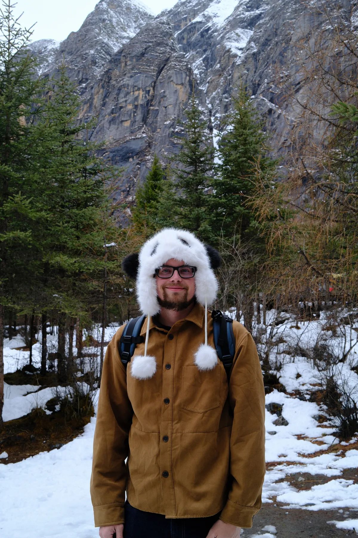 Lewis standing in a snowy mountain valley wearing a furry white hat.