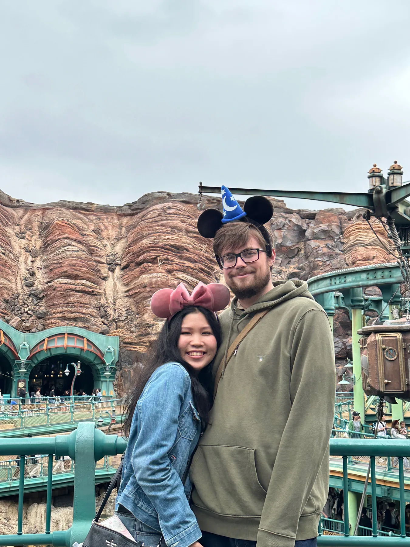 Lewis and Gail wearing character ears beside a rocky water attraction.