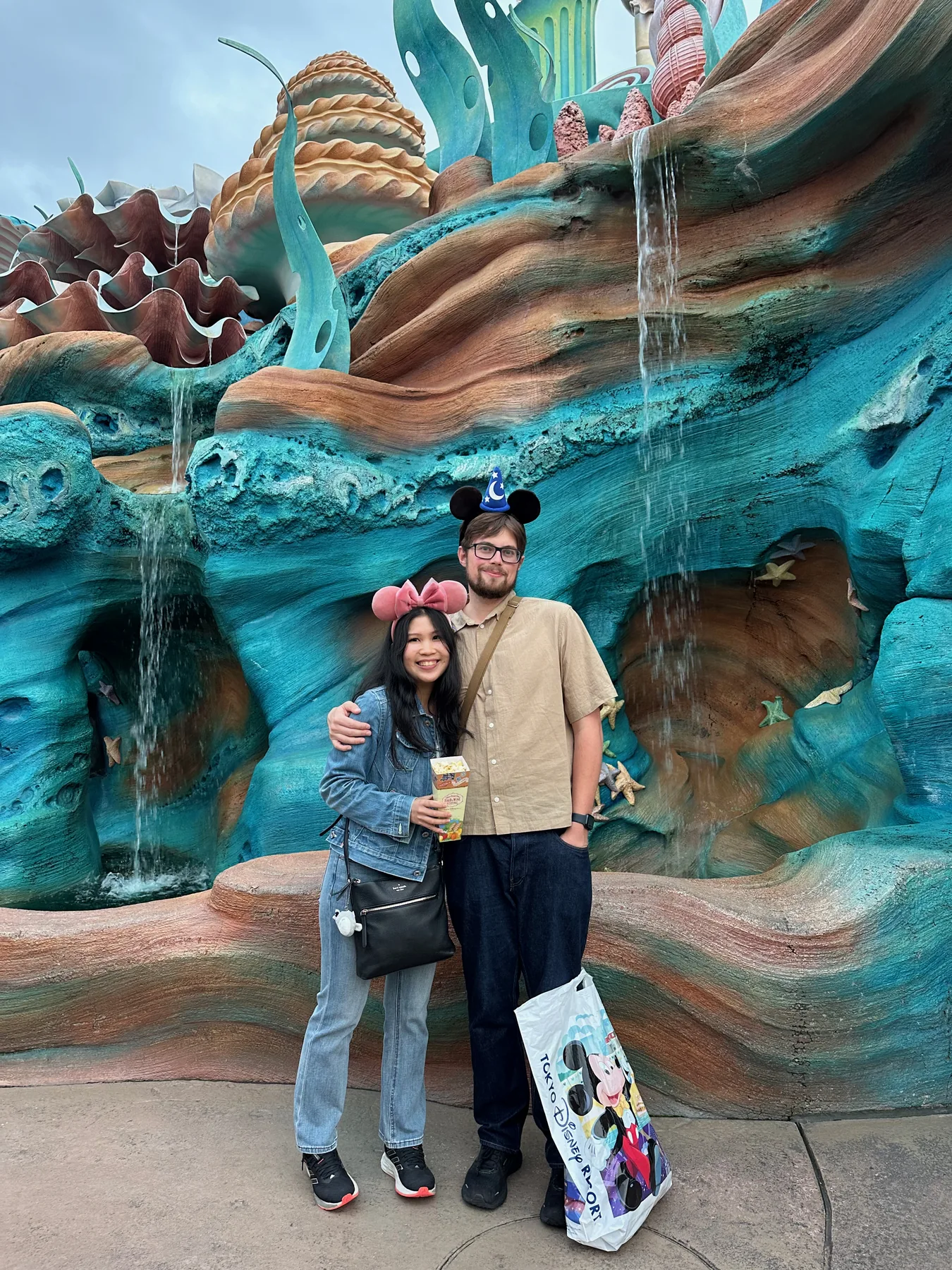 Lewis and Gail standing together in front of a colourful sculpted rock fountain.