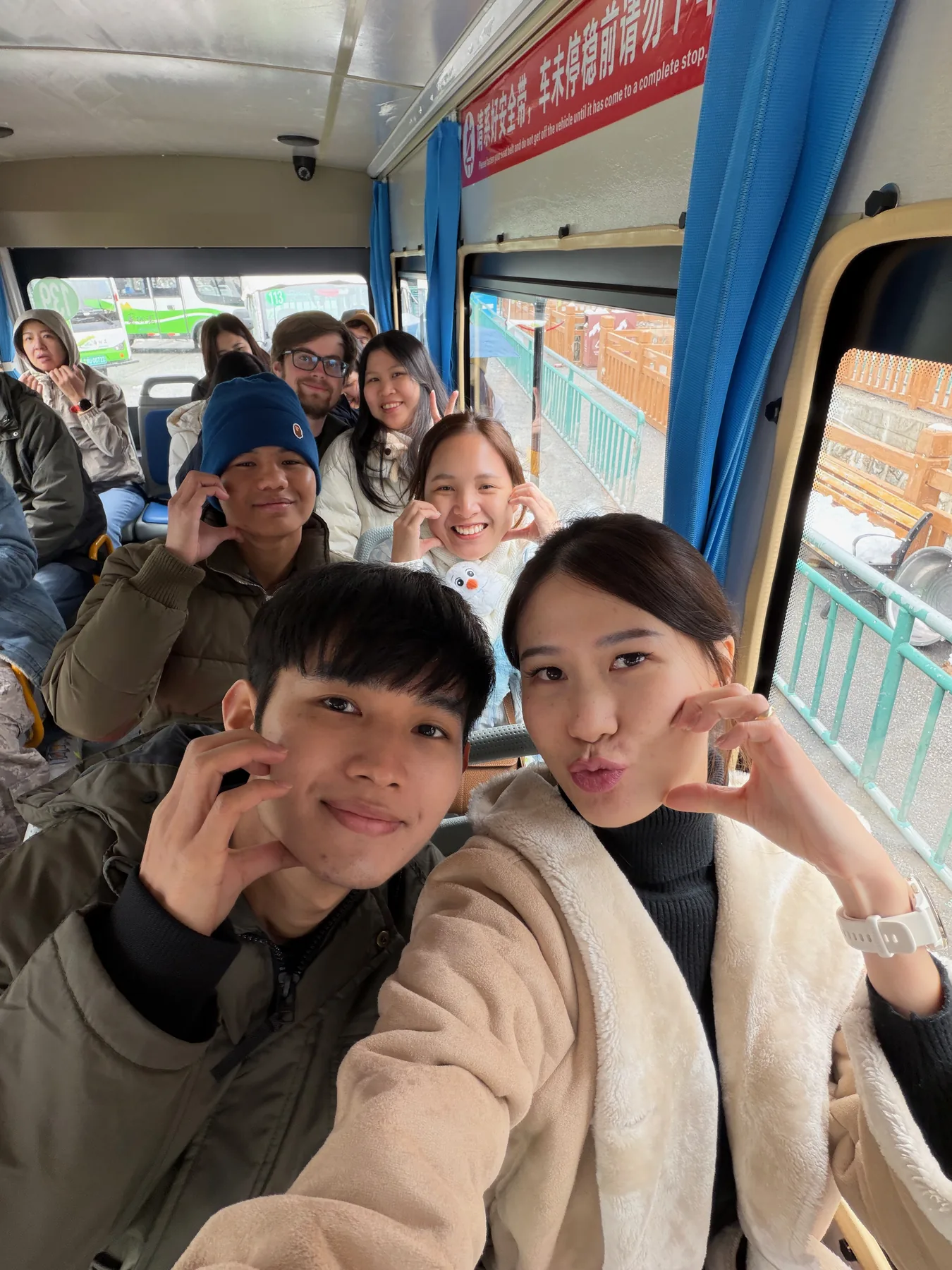 Lewis and Gail smiling from the back row of a group selfie on a bus.